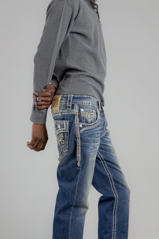 Person wearing a gray sweater and blue jeans with intricate designs on a plain background