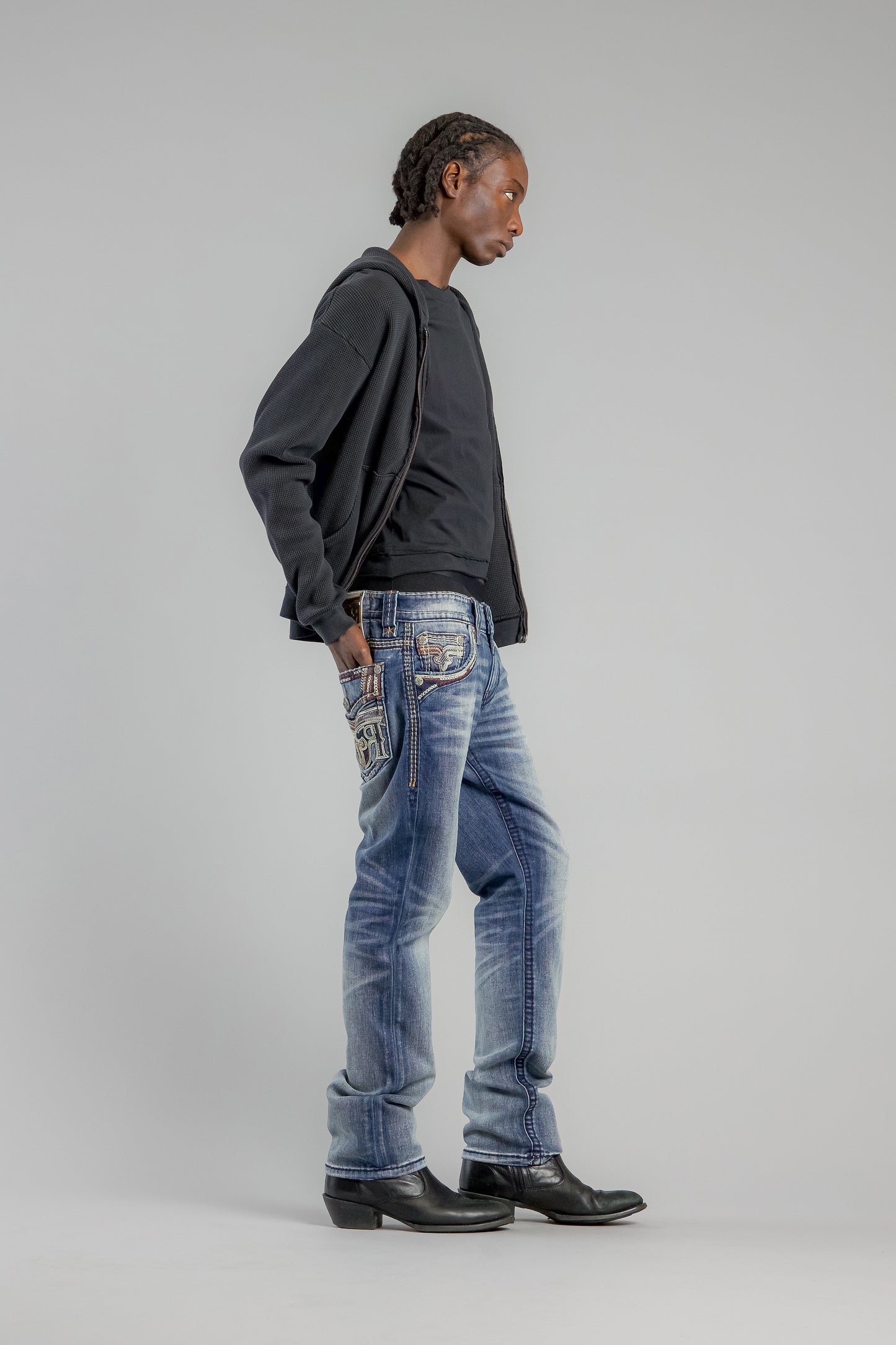 Person wearing blue jeans and a dark hoodie on a plain background