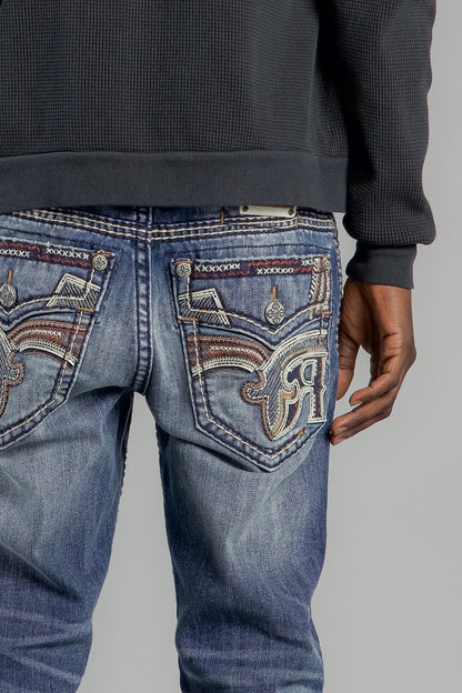 Close-up of blue jeans with intricate patterns on the back pocket against a gray background.